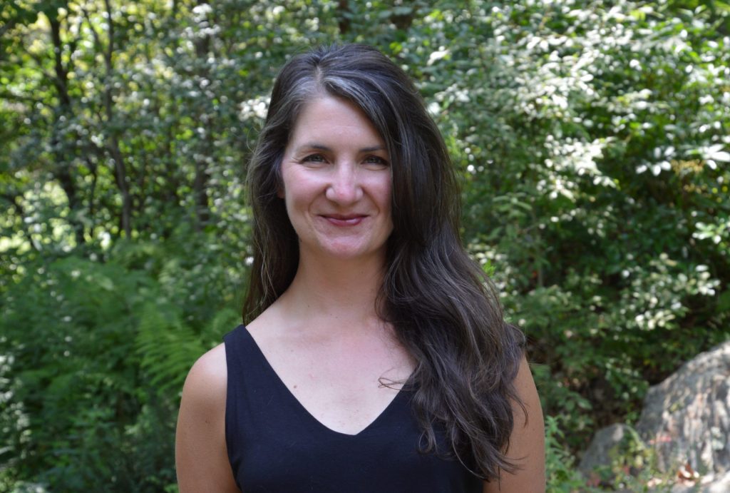 Portrait of a woman in a black shirt with long hair with trees behind her. Katie Blake. Staff Interview