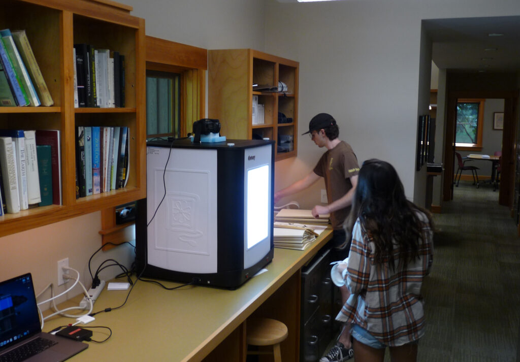 Two students work in an open office and around a large light box and mounted camera. Highstead's Herbarium.