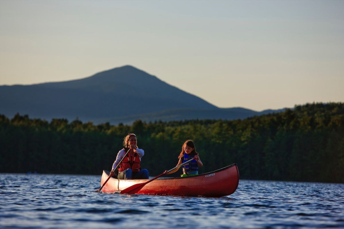 A woman and a young girl canoe on a lake with mountains in the background. Conservation Finance.