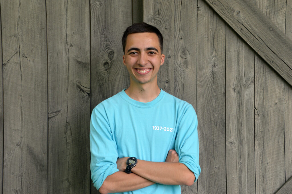 A man stands with his arm crossed and smiles in front of a wooden wall. Beau Martinez, 2022 Yale Conservation Scholar, University of Notre Dame