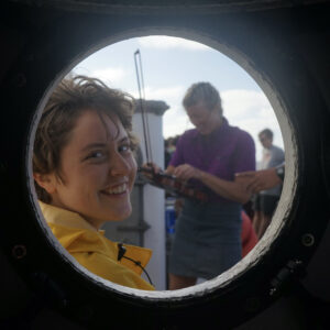 A woman smiles through a porthole window. Behind her, another woman plucks a violin. A Q&A with Highstead’s New Conservation Interns